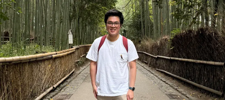 Gary smiles for the camera while standing on a path surrounded by trees.